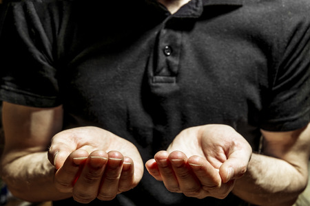 A man in a black t-shirt stands with outstretched handsの写真素材
