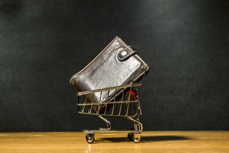 wallet in a miniature grocery cart on a wooden surface on a dark backgroundの写真素材
