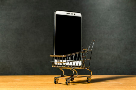 Smartphone in a miniature grocery cart on a wooden surface on a dark backgroundの写真素材