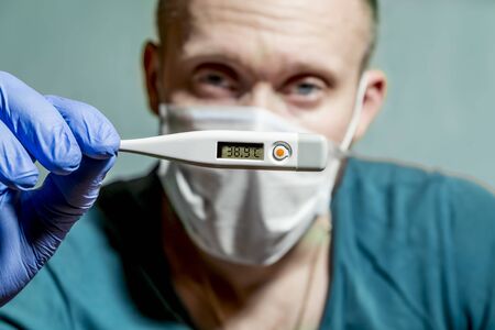 A medic wearing a protective mask and gloves holds a thermometer to measure body temperatureの写真素材