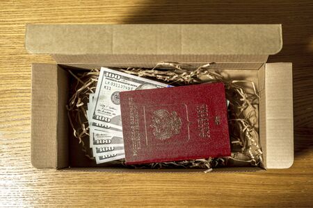 One hundred dollar bills enclosed in a russian foreign passport lie in a cardboard box on a wooden surfaceの写真素材