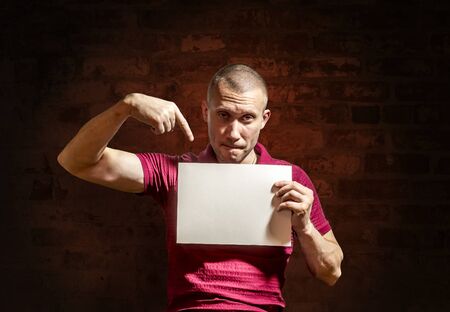 The man points to a white sheet in his hand against a brick wallの写真素材