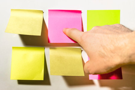 The index finger points at the Colored square  notes pasted on the white wall in the officeの写真素材