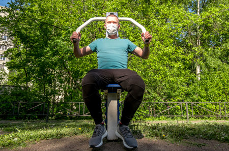 A man in a medical mask trains on sports equipment in a courtyard in the city during the pandemic