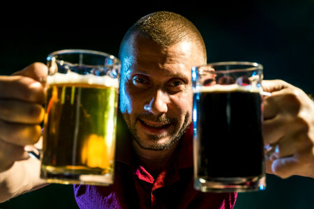 Satisfied man with light and dark beer in mugs on a dark green background
