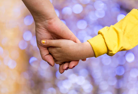 A woman's hand holding the hand of a little girl against the background of bokehの写真素材