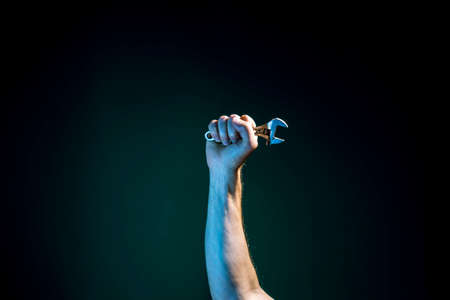 A raised Male hand holds a spanner on a dark green backgroundの写真素材