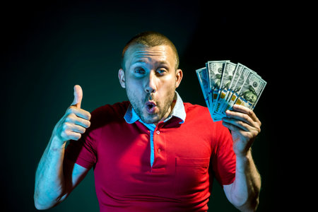 A happy Man with a fan of hundred dollar bills poses on a dark green background