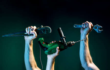 Raised male hands hold a spanner and a puncher on a dark green backgroundの写真素材