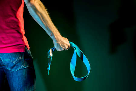 Aggressive man holding a belt in his hand on a dark green backgroundの写真素材