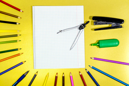 Stationery and multicolored pencils with a notebook are spread out on a yellow surface