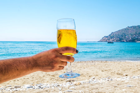 A woman holds a glass of cold beer against the hot seascape at the resort
