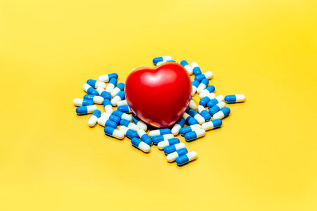 Scarlet toy heart among medicinal capsules lies on a yellow background