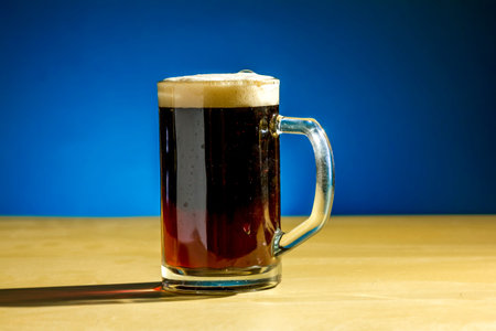 A mug of dark beer stands on the table on a blue background
