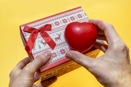 Man's hands hold a box with gifts and toy red heart on a yellow backgroundの写真素材