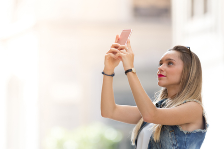 Pretty blonde teenager taking a photo with her mobile phoneの写真素材