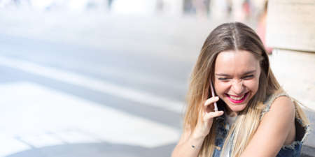 Pretty and happy blonde teenager outdoor talking on her mobile phoneの写真素材