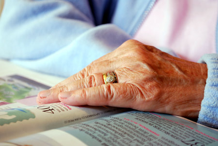 closeup of a hand of an eldery woman reading on a magazine