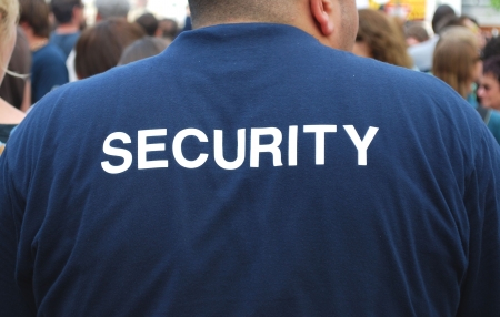 back of a security guard watching a crowd of peopleの写真素材