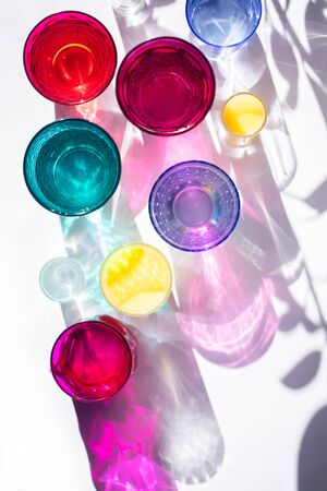 Glass goblets create wonderful coloured shadows on a solar table. The shadow of sunlight reflect to glass of pink and yellow, emerald colors. Top viewの写真素材