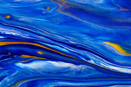 Fluid art texture. Abstract backdrop with swirling paint effect. Liquid acrylic picture with beautiful mixed paints. Classic blue color of the year 2020. Blue, golden and white overflowing colors.の写真素材