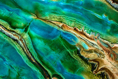 A fluid art texture is created by combining colored paints. An abstract liquid background with colorful waves and swirling forms. The bright wavy backdrop is made by mixing the dyes or paints.の写真素材