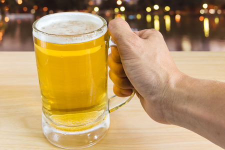 man hand holding frosty glass of light beer for drinking on wooden with blurred backgroundの写真素材