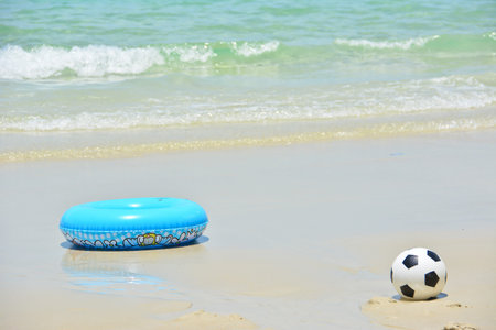blue swim ring and football on the beachの写真素材