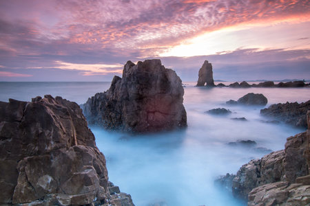 Sunset beach has waves breaking on the rock beach with a color filled sky