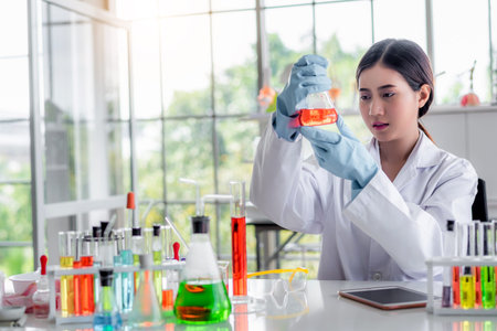 Attractive young Asian scientist woman lab technician assistant analyzing sample in test tube at...