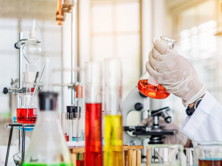 hand of scientist holding flask with lab glassware and test tubes in chemical laboratory background, science laboratory research and development conceptの写真素材