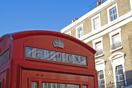 Red telephone booth in London over blue sky and in front of buildingの写真素材