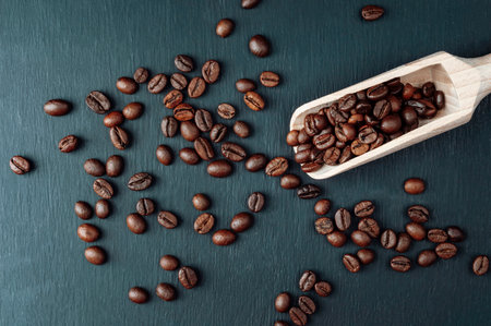 Coffee beans and wooden spoon. coffee beans on a dark . Concept: export and import of coffee beans, coffee consumption. scattered fresh roasted coffee grains with copy space for advertisementの写真素材