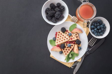 Stack of Belgian waffles with blueberry and honey for breakfast. Delicious homemade pastry. Waffles with raspberries, blueberries, sour cream and honey. Waffles on the table. Flat lay top view.の写真素材