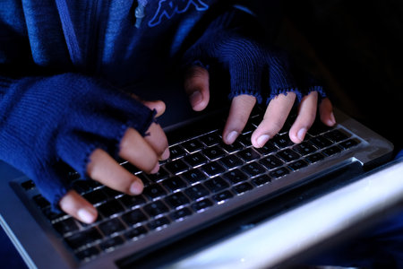Close up of Hooded hacker steeling data from laptop