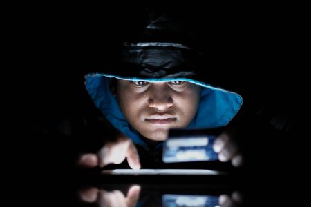 hooded hacker sealing data from laptop at nightの写真素材