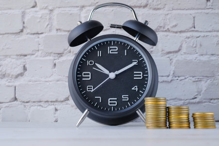 Close up of alarm clock and stack of coin on table.