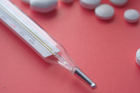Close up of thermometer and pill on red background