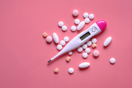 close up of pills and thermometer on pink background