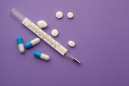 close up of pills and thermometer on purple background .の写真素材