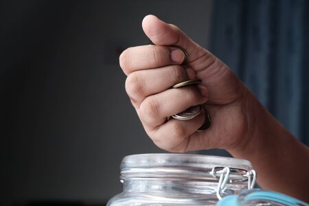 Close up of women hand saving coin in a jar.の写真素材
