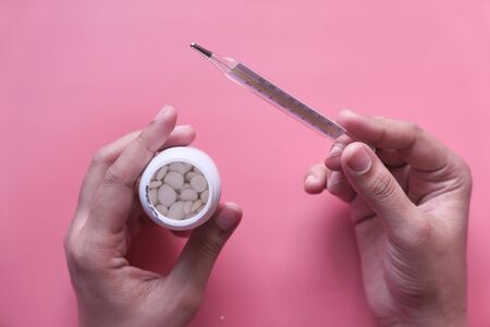 cropped woman holding plastic container and thermometer on pinkの写真素材