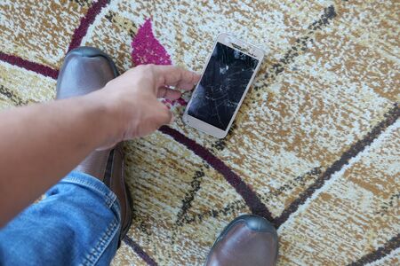 man hand picking broken smart phone from floorの写真素材
