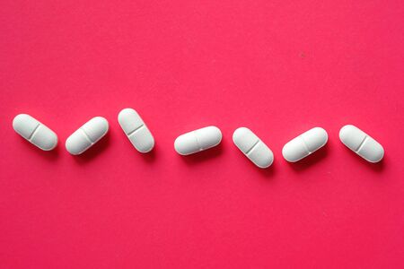 close up of white pills spilling on a red backgroundの写真素材