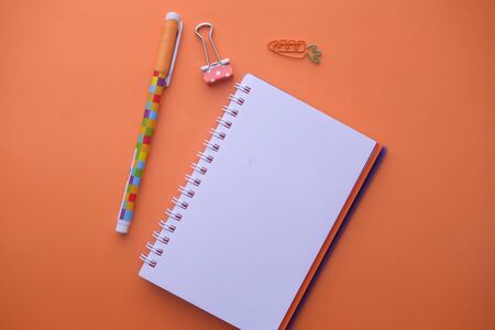 Wide view of blank spiral note pad and pen on orange color backgroundの写真素材