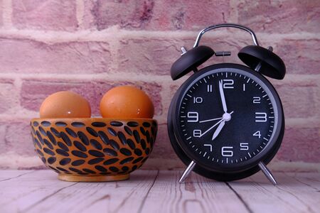 alarm clock and eggs in a bowl on tableの写真素材
