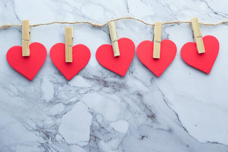 Clothes pegs and red wooden hearts on rope isolated on white background