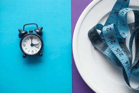 A clock on the plate and tape measure, Intermittent fasting diet conceptの写真素材