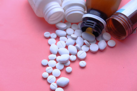 color pills spilling from container on pink background, top view