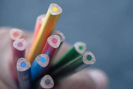 child hand holding color pencils on table.